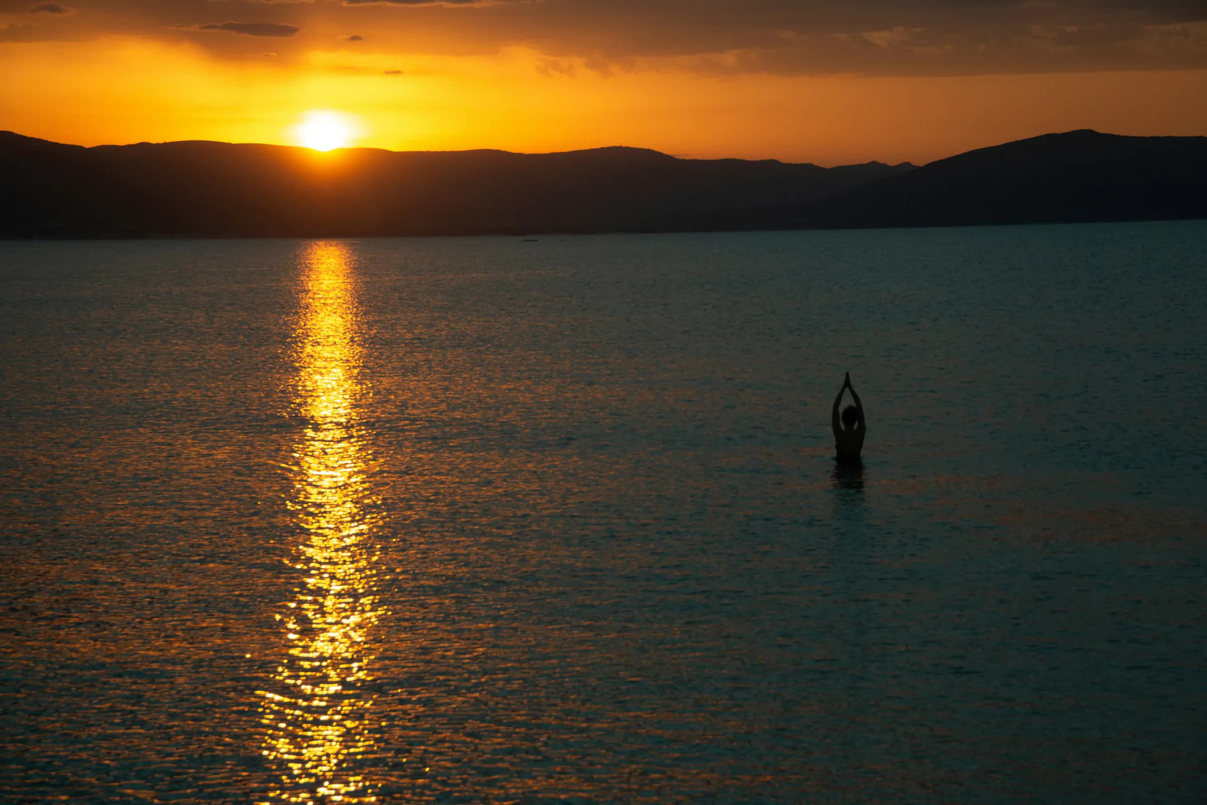 A person practicing yoga in a lake at sunset