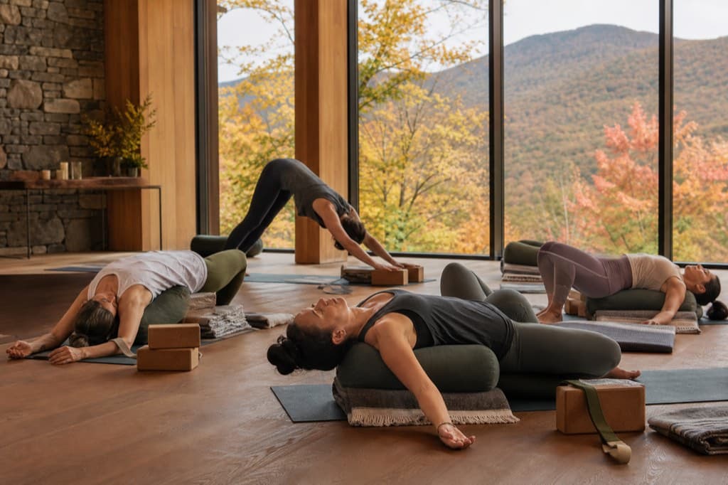 Yoga practitioners using bolsters and blocks in a refined Catskills studio surrounded by autumn foliage