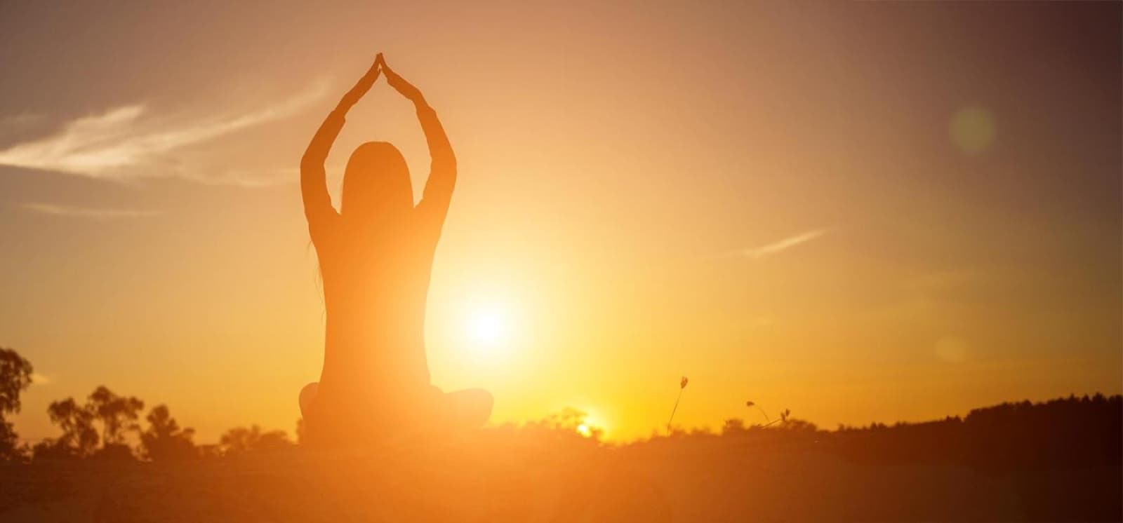 A seated yoga practitioner silhouetted against warm sunset light in Omega's official Energy Medicine Yoga image