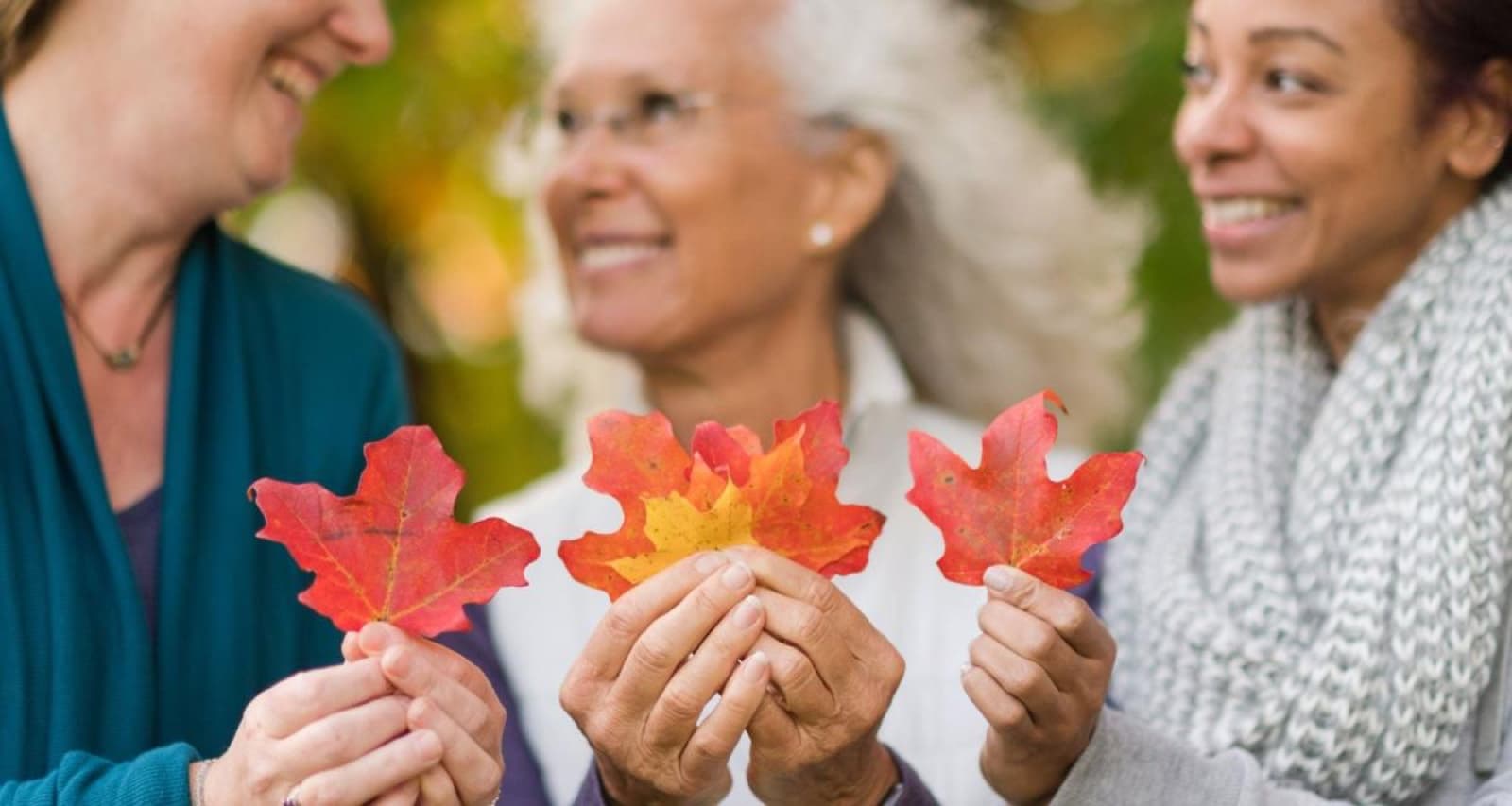 Three retreat participants holding vivid autumn leaves in Kripalu's official Fall Ayurveda program photograph